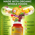 Supplements Studio Quercetin with Bromelain, Vitamin C, and Zinc bottle surrounded by organic whole foods like acerola cherries, pineapple, apple, onion, grapes, broccoli, ginger, orange, and lemon, shown inside a capsule to highlight food-based formulation.